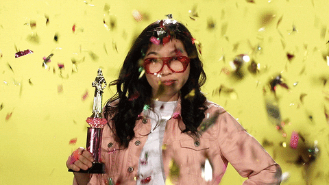 Woman holding a trophy while confetti is falling from above gif